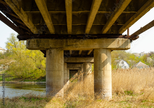 Concrete bridge dilapidated pillars. Overpass seen from below showing support beams. Bridge over river © MTX