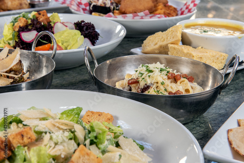 Full table of a variety of restaurant dishes to choose from with macaroni and cheese bowl in the center.