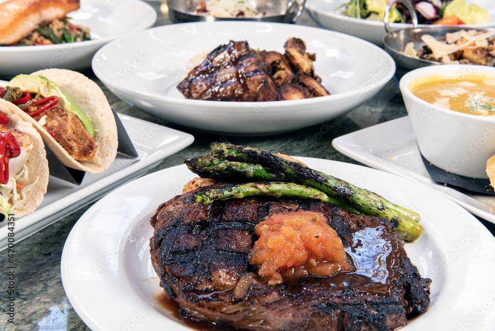 Full table of a variety of restaurant dishes to choose from with rib eye steak in the center.