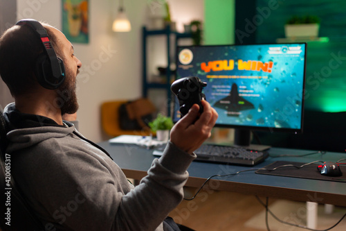 Videogame player raising hands after winning space shooter competition wearing headset. Professional pro gamer playing online videogames with new graphics on powerful computer from gaming room
