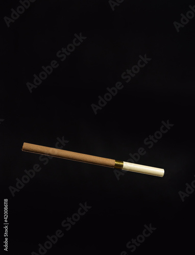 An unlit brown cigarette with a beige mouthpiece on a dark background.