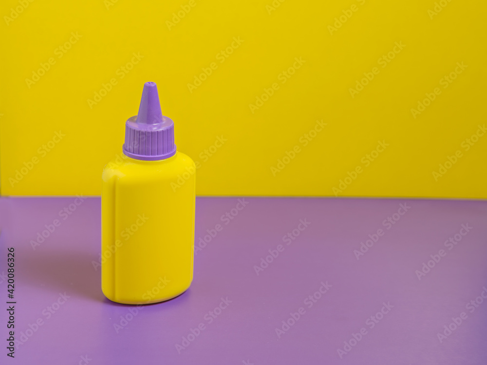 Yellow bottle with purple cap stands on purple table with yellow background
