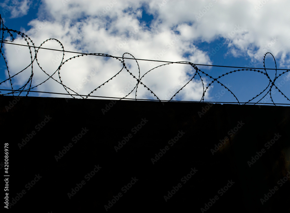 Stone wall with barbed wire against blue sky. Space for text Stone wall with barbed wire against blue sky. Space for text