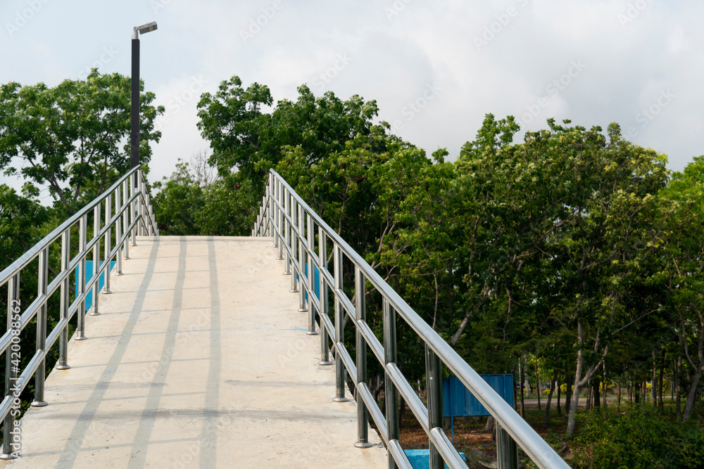 An elevated cement bridge with steel handrails for crossing the river inside the park. Landmark at Kodpor Public Park, Rayong ,Thailand.