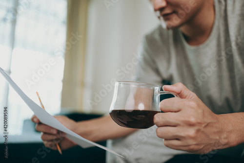 Young Businessman working at home with paper graph and data sheet and he is dirnk coffee. Business and freelance concept. photo