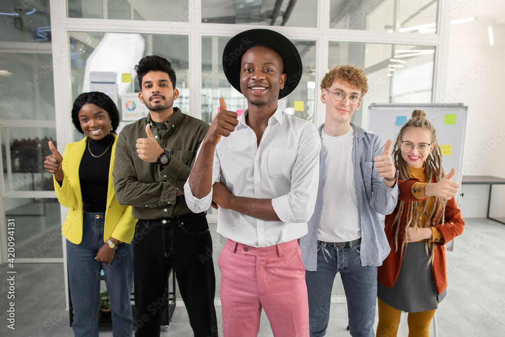 Smiling multiracial students showing thumbs up at office