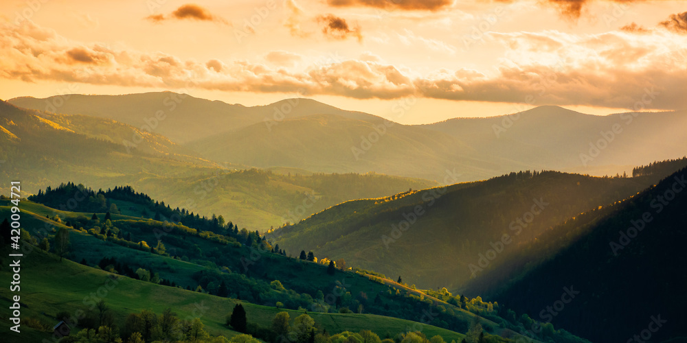 mountainous countryside scenery at sunset. dramatic sky above the distant valley. green fields and trees on the hill. beautiful nature scenery of carpathians