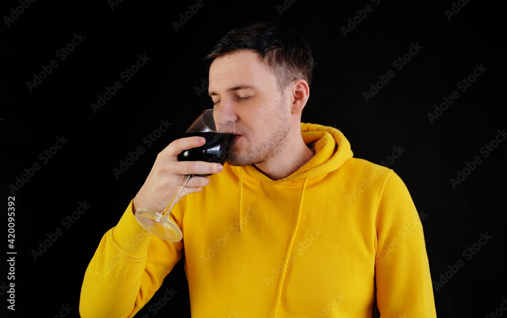 Relaxed young man poses with glass of red wine on black background. Adult happy guy resting with alcohol in his weekend. Relaxed young man poses with glass of red wine on black background. Adult happy guy resting with alcohol in his weekend.
