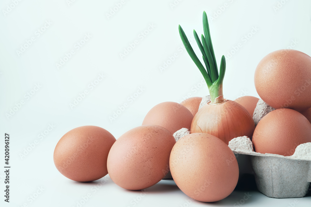Heap of brown eggs and green onions. Green onions in middle of brown raw chicken eggs in an egg box on a light background. Concept of dietary and healthy natural protein products. Heap of brown eggs and green onions. Green onions in middle of brown raw chicken eggs in an egg box on a light background. Concept of dietary and healthy natural protein products.