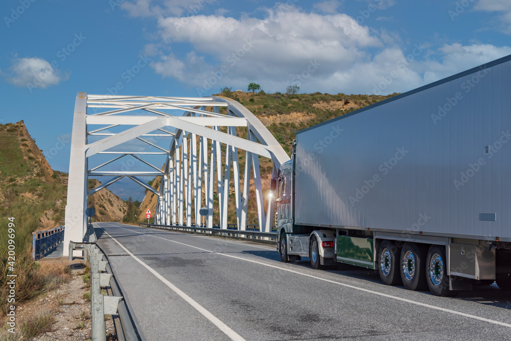 Truck with refrigerated semi-trailer on a mountain road and going over an iron bridge.
