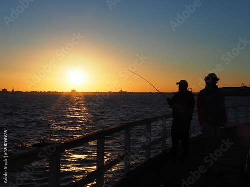 People fishing at the Pier and sun is setting in the backdrop . Location Lagoon Pier in Port Melbourne, Victoria , Australia