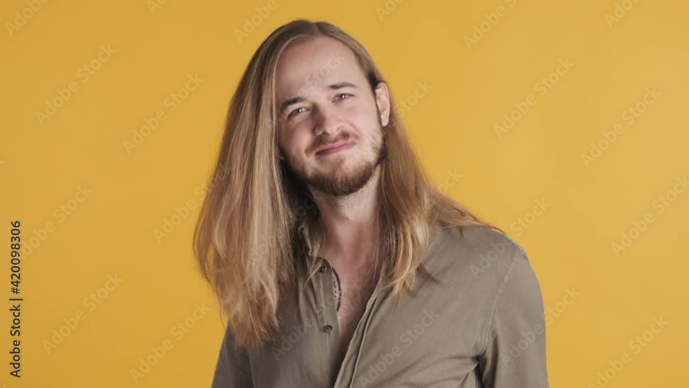 Young long haired guy looking impressed keeping thumb up on camera over yellow background. Like it gesture Young long haired guy looking impressed keeping thumb up on camera over yellow background. Like it gesture