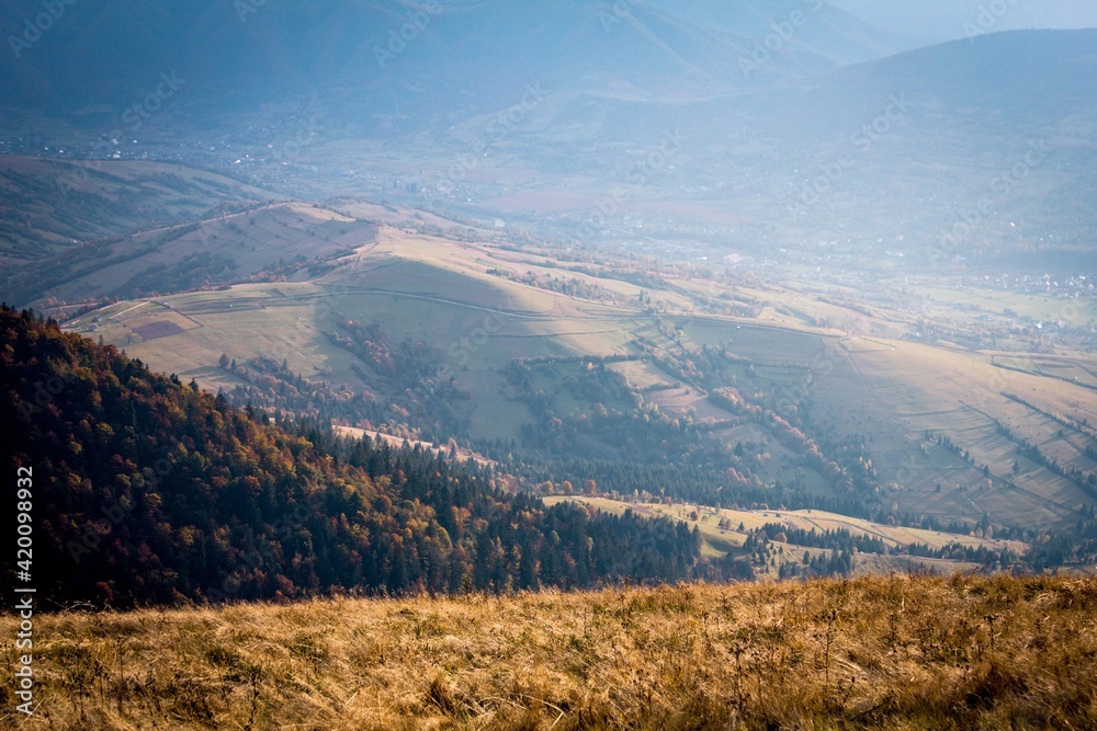 Mountain landscape. View from the top to a village in a valley. Photo in autumn golden colors with a haze.