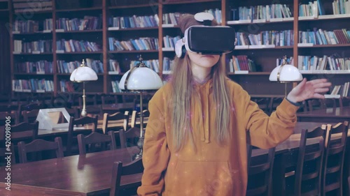 Pretty teenage schoolgirl standing in school library wearing virtual reality glasses vr headset for studying playing video games watching educational video feeling excited. Technologies for education. photo