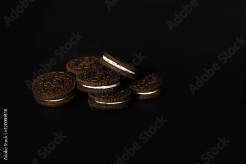 Round chocolate cookies with cream filling on a black background.