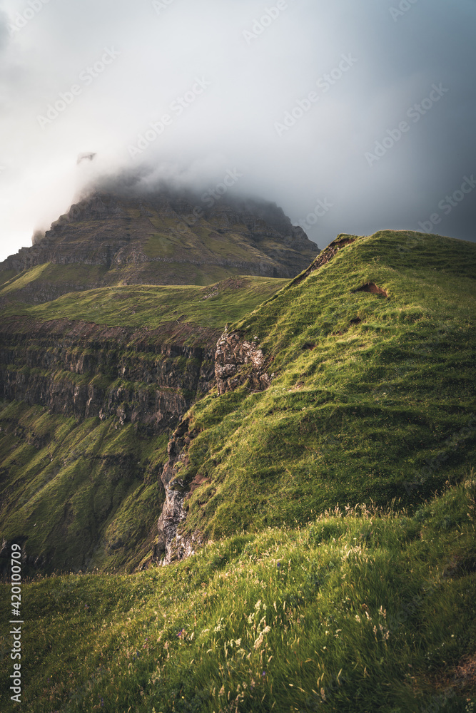 Faroe islands with stormy view towards mykines on the island of Vagar as seen from mulafossur waterfall. Low clouds with atlantic ocean waves.
