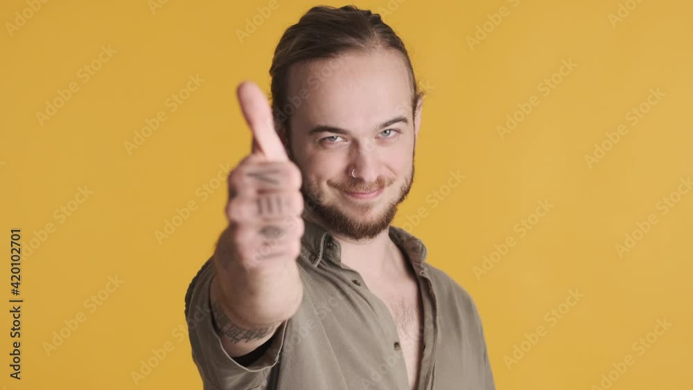 Attractive smiling bearded guy keeping thumb up approving your choice isolated on yellow background. Nice job expression Attractive smiling bearded guy keeping thumb up approving your choice isolated on yellow background. Nice job expression