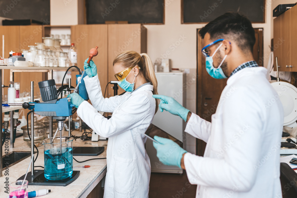 Fototapeta premium Middle age scientists and researchers with face protective masks work in chemical laboratory on coronavirus vaccine.