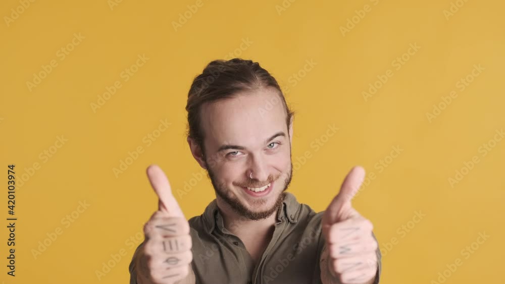 Attractive smiling bearded guy keeping thumbs up showing like it expression isolated on yellow background. Nice job expression Attractive smiling bearded guy keeping thumbs up showing like it expression isolated on yellow background. Nice job expression