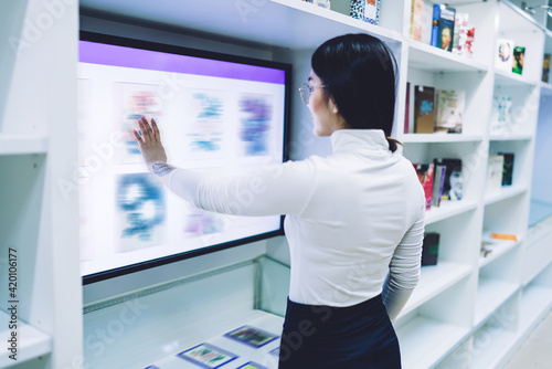 Young woman standing in front of touch screen and selecting book