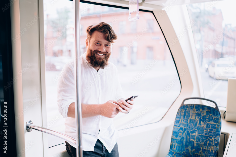 Young bearded man with smartphone smiling in train Young bearded man with smartphone smiling in train