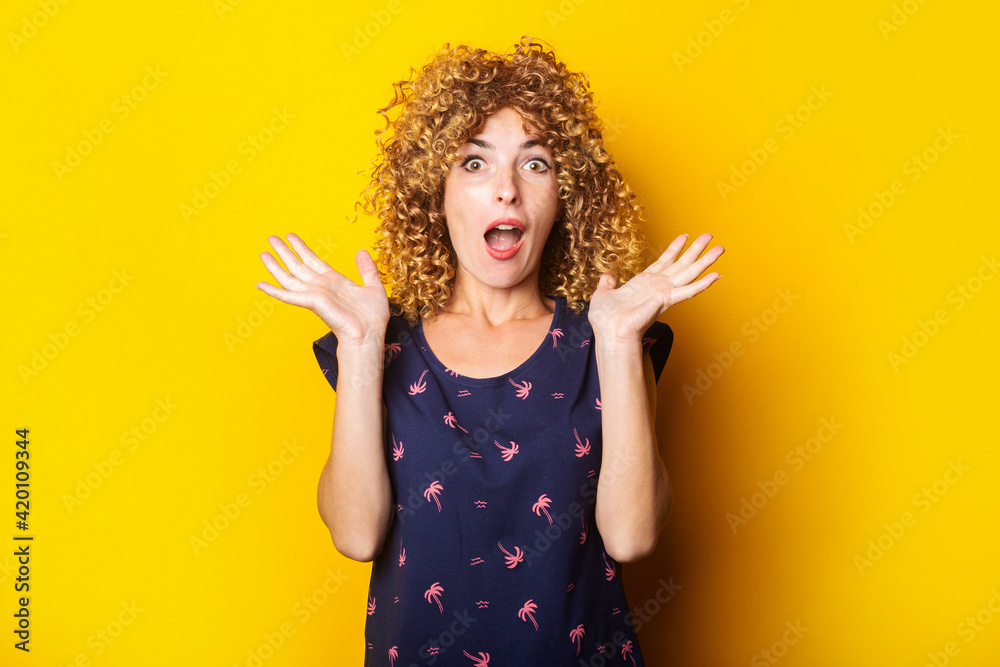 shocked surprised beautiful curly young woman on a yellow background. shocked surprised beautiful curly young woman on a yellow background.