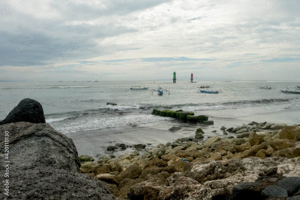 The atmosphere in the morning at Matahari Terbit Beach, Sanur, Bali, Indonesia. There are waves crashing against rocks, fishing boats and beach watchtowers
