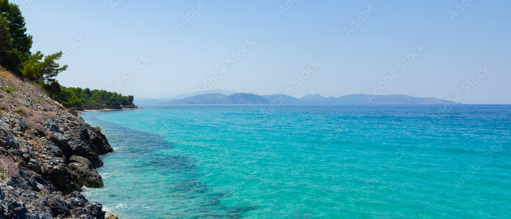 Seascape with mountains. Flowers and trees on the rocky shore. View of the rocky coast and turquoise sea water. Summer vacation concept by the sea. Copy space Seascape with mountains. Flowers and trees on the rocky shore. View of the rocky coast and turquoise sea water. Summer vacation concept by the sea. Copy space
