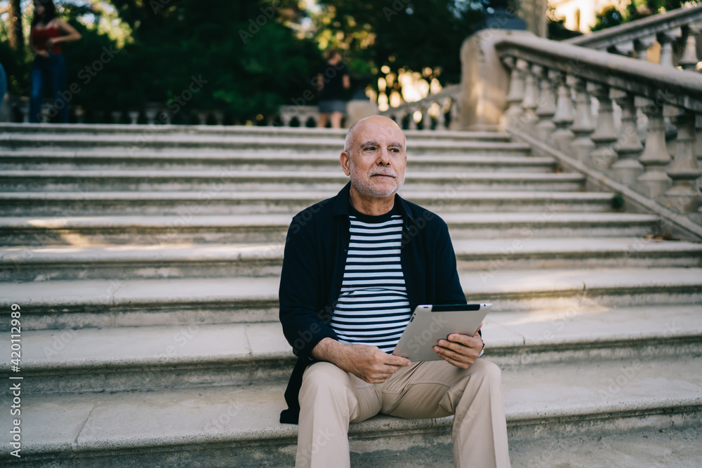 Pensive male tourist resting at ancient stairs in city feeling pondering on travel lifestyle, contemplative senior with modern digital technology for make booking thinking about vacations outdoors Pensive male tourist resting at ancient stairs in city feeling pondering on travel lifestyle, contemplative senior with modern digital technology for make booking thinking about vacations outdoors