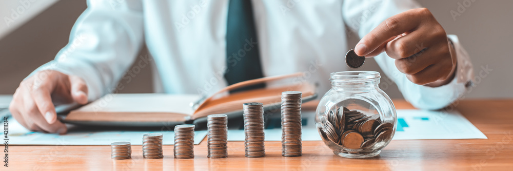 © Puwasit Inyavileart - Financial businessman with coins put in a jar, Saving money for future growth and knowing how to manage your spending wisely, Saving money for business growth or long-term profitability.