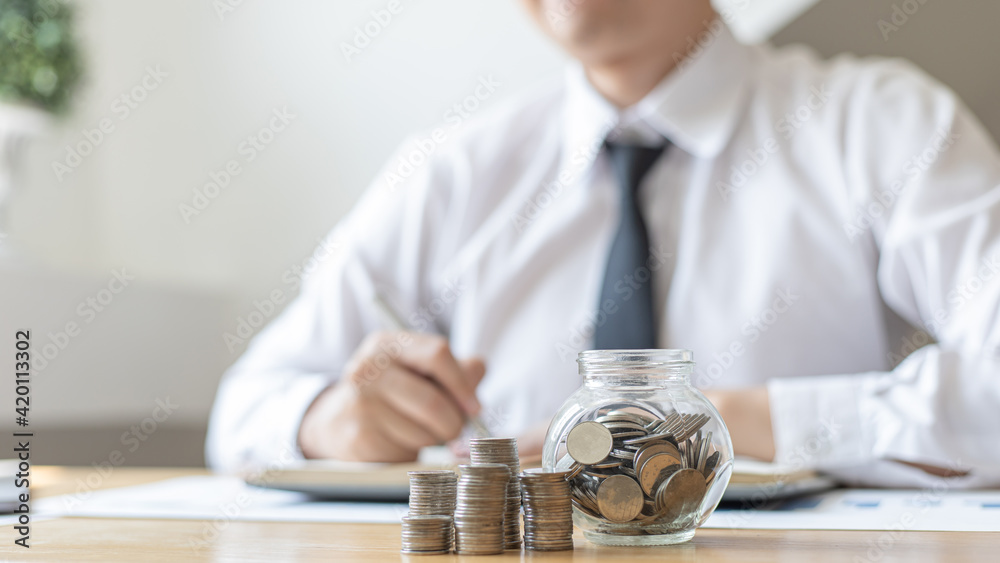 Dollar coins arranged in a slope graph, Blurred image of a businessman pressing a calculator, Financial business growth, Saving money for business growth or long-term profitability, Save money.