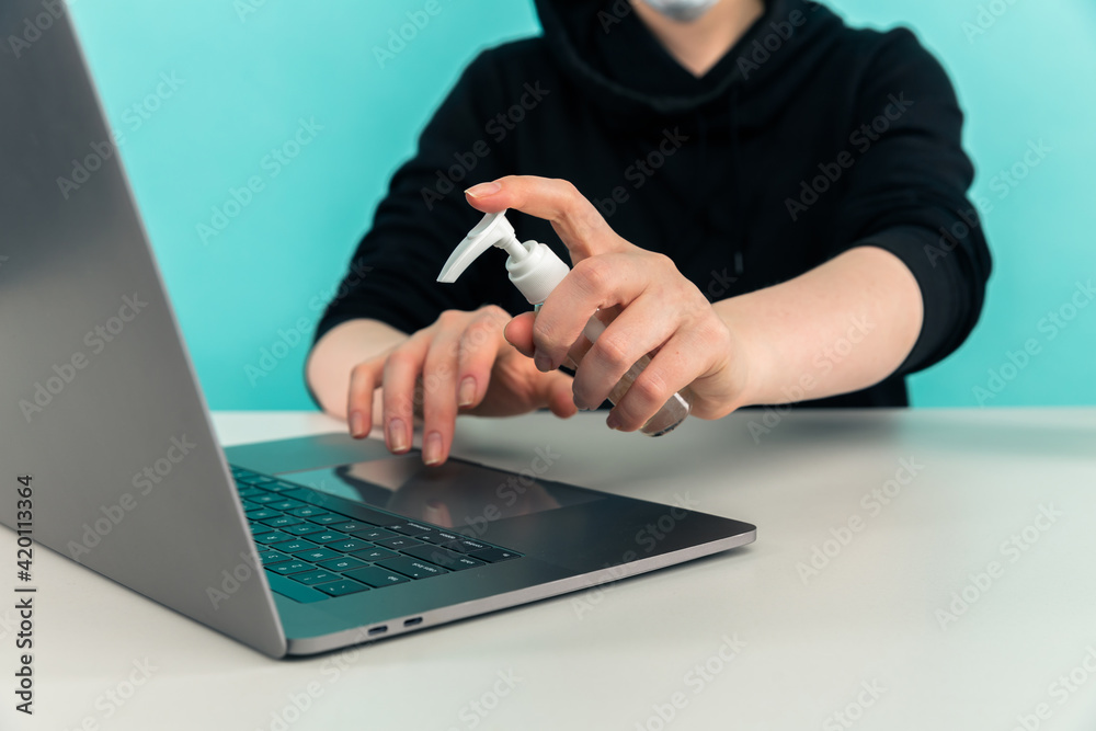 Woman in the mask desinfecting hands and laptop at home. Woman in the mask desinfecting hands and laptop at home.