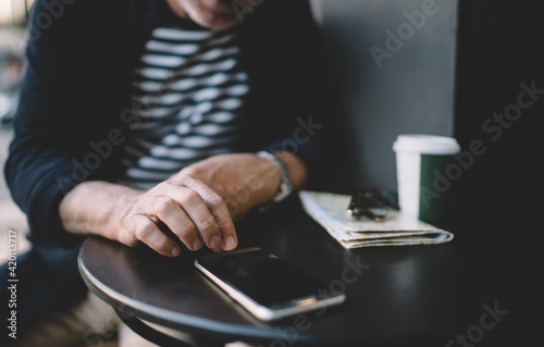 Unrecognizable male blogger checking time on modern cellphone gadget while resting in street cafe, cropped man using smartphone application for installing notification during wireless browsing