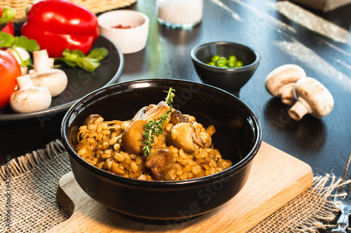 Fotografi Pearl barley risotto or orzotto with mushrooms in dark bowl on wooden background