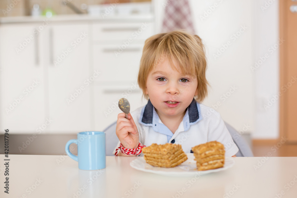 Cute preschool boy, blond child, eating piece of cake and drinking milk at home Cute preschool boy, blond child, eating piece of cake and drinking milk at home