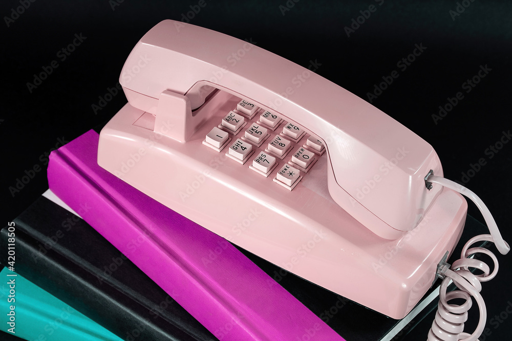 Close up of retro pink telephone on a stack of hardcover books isolated on black Close up of retro pink telephone on a stack of hardcover books isolated on black