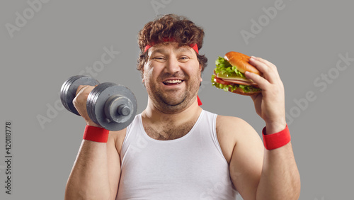 Fotografie Funny smiling man with dumbbell and delicious burger looking at camera