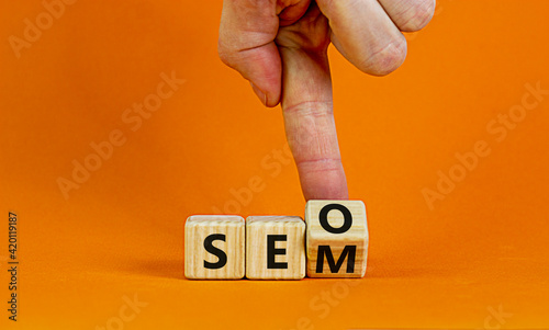 SEO vs SEM symbol. Businessman turns a cube and changes words SEO, Search Engine Optimization to SEM, Search Engine Matketing. Business, SEO vs SEM Concept. Beautiful orange background, copy space. photo