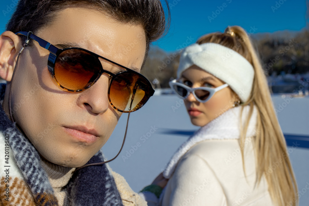 Portrait of a young couple in advertising style, wearing sunglasses and winter clothes on a cold but sunny day