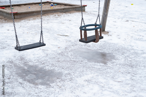 Slippery kids playground in public park during winter. Frozen ice under the swings.