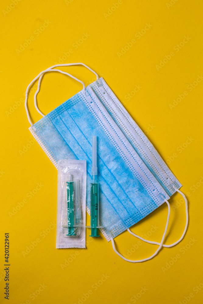 Medical face mask and Syringe isolated in yellow color background.