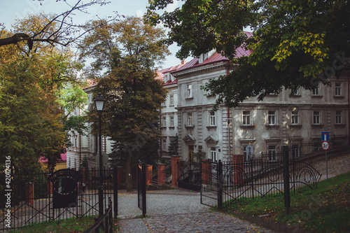 A small cozy Zamkova Street in Przemysl, leading from Casimir Castle. Cobblestones street with old beautiful buildings, tall trees in the autumn park and fallen leaves on sunny day in Poland.  photo