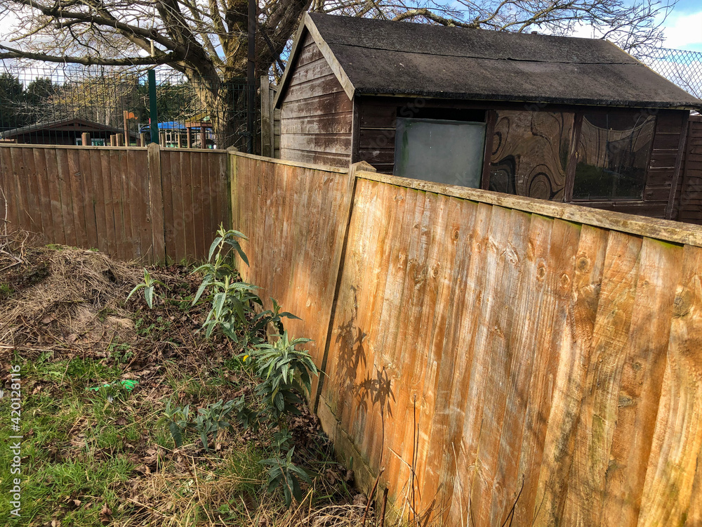 A broken fence post in a garden is causing the fence to lean and look wonky.