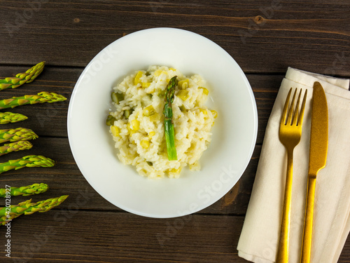 Risotto with asparagus. Dish with creamy rice with asparagus. Mediterranean food. Plate with cutlery, fork and knife. Spring recipe. Rustic wooden table. Flat lay. Top view. 