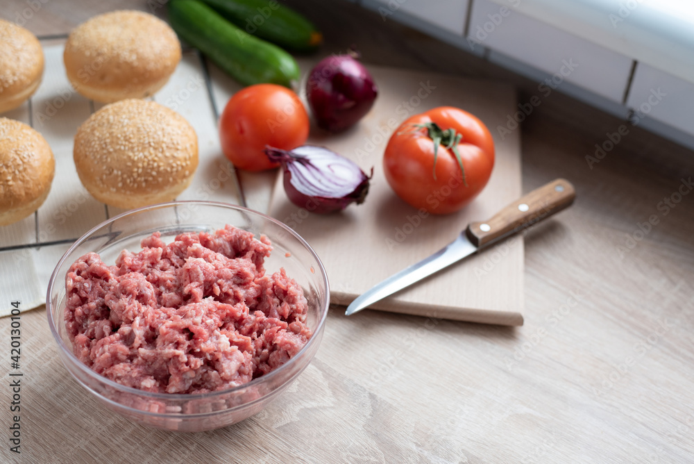 Ground beef in a glass bowl on the kitchen table with other hamburger ingredients, cooking at home. Ground beef in a glass bowl on the kitchen table with other hamburger ingredients, cooking at home.