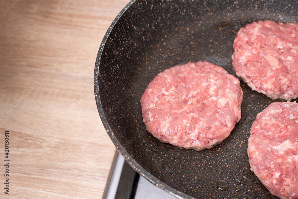 Three raw beef patties grilling in a non-stick frying pan in the kitchen.