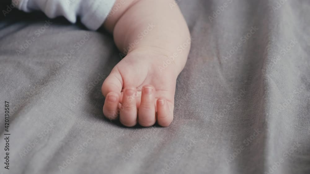 Close up of tender little infant child baby kid hand with five fingers lying on cozy grey bed at home. Baby skincare concept Close up of tender little infant child baby kid hand with five fingers lying on cozy grey bed at home. Baby skincare concept