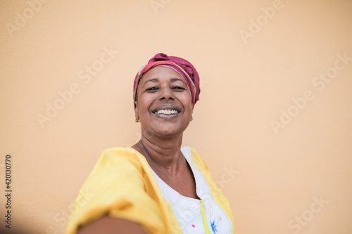 Happy black senior woman taking a selfie while smiling in camera - African person wearing traditional dress and turban