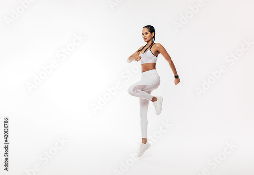 Young fit woman exercising over white background. Female in white sportswear jumping indoors.