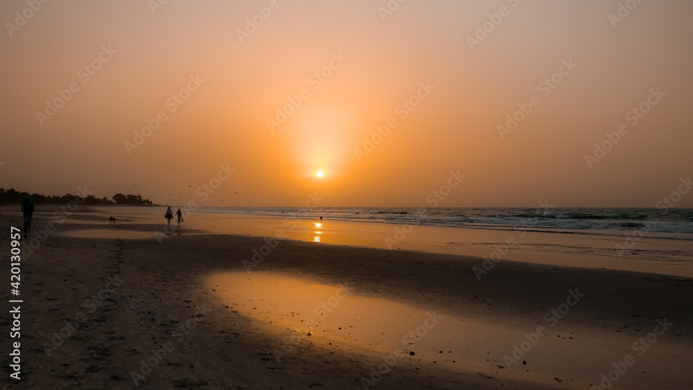 Naklejka premium African beach orange sunset. People / community get together at the evening time. Kotu beach, The Gambia